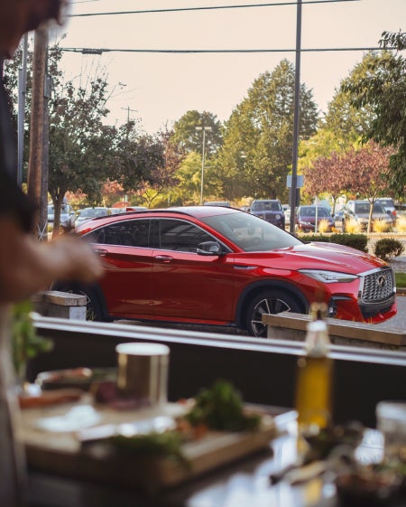 A red INFINITI vehicle parked outside a restaurant window.