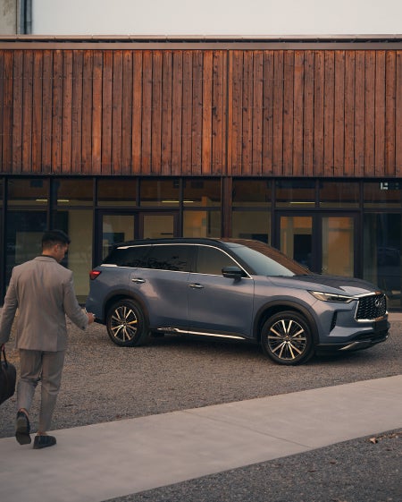 A man approaching his blue INFINITI SUV parked in front of a modern building.